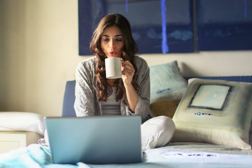 Woman working from home on bed with laptop and coffee cup