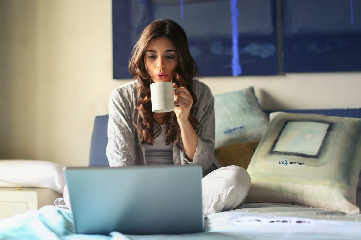 Woman working from home on bed with laptop and coffee cup
