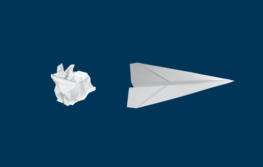 Balled up piece of paper next to a paper airplane on dark blue background