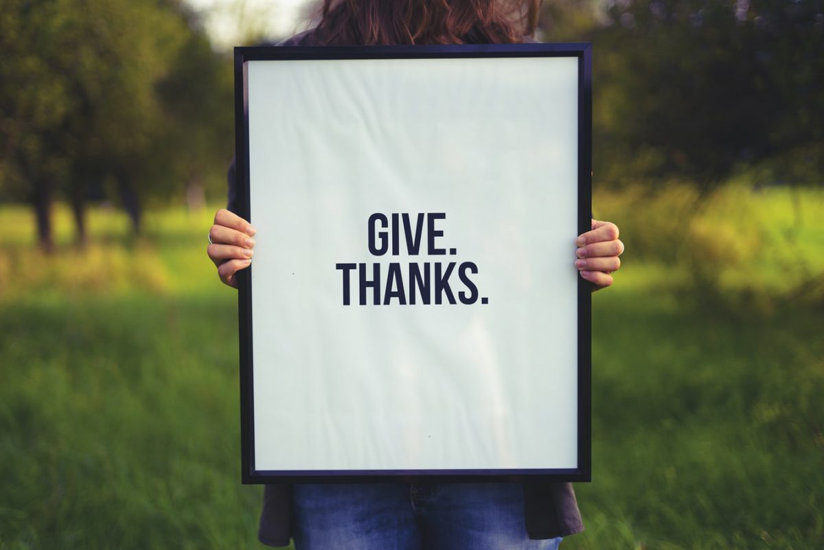 Woman practicing gratitude by holding a framed poster that says Give. Thanks.