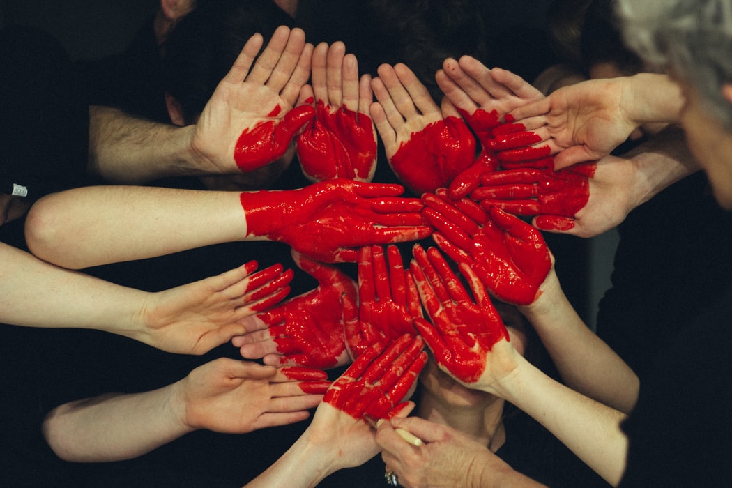 Red painted hands of employees gathered into the shape of a heart showing team collaboration